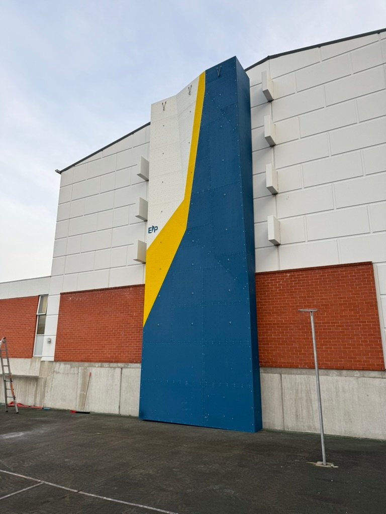 A tall custom outdoor climbing wall built by ClimbCraft on a school building