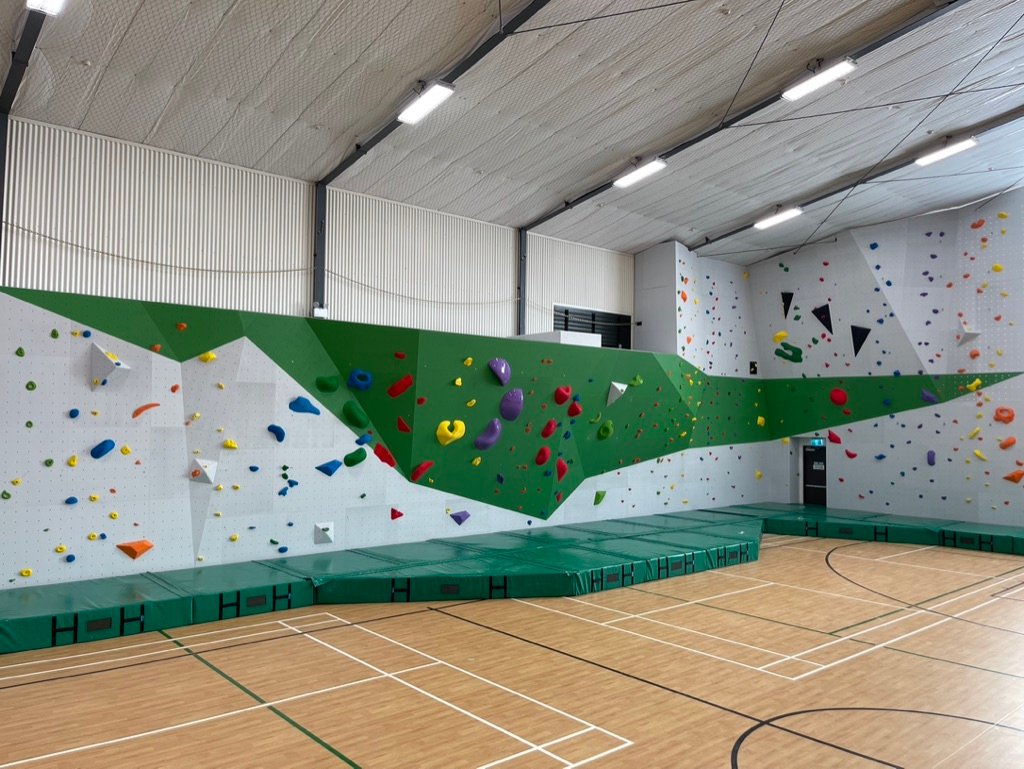 Large green and white school bouldering wall in a sports hall at Dilworth School
